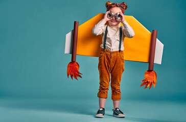 Smiling child with paper plane wings and eyeglasses isolated on blue