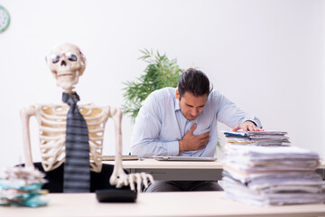 Obraz premium Young male employee and skeleton in the office