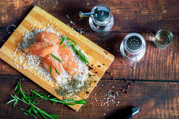 Chicken jerky lies on a board with spices and sea salt. Rosemary, cardamom, pepper.