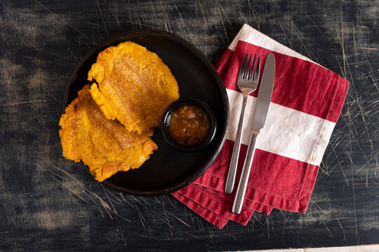 Plato de patacones colombiano con salsa de tomates y cebolla hogao. Persona comando plato tradicional latino. Platano pisado aplastado.