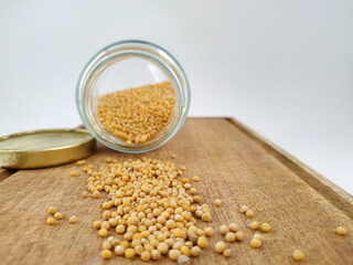 side view of mustard grains on a wooden board on a white background