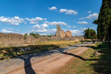 Via Appia Antica, in summer between clouds, blue sky and the shadows of the trees. Next to the ruins of Villa dei Quintili. This road connected Rome to Brindisi. Italy. Maritime pines and cypresses