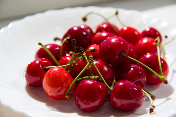 A handful of cherries lies on a white plate.