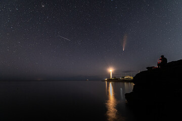 Person smoking and looking at Neowise comet over white Lighthouse at night sky