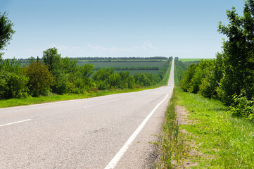 suburban empty road asphalt surrounded by trees and grass. The concept of transportation and travel. Background green grass asphalt and blue sky
