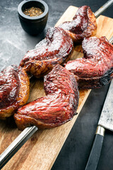 Barbecue dry aged wagyu Brazilian picanha from the sirloin cap of rump beef offered as closeup on a skewer on a wooden board on black background