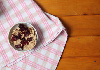 a bowl of cornflakes and dry berries on a towel on wooden background flat lay