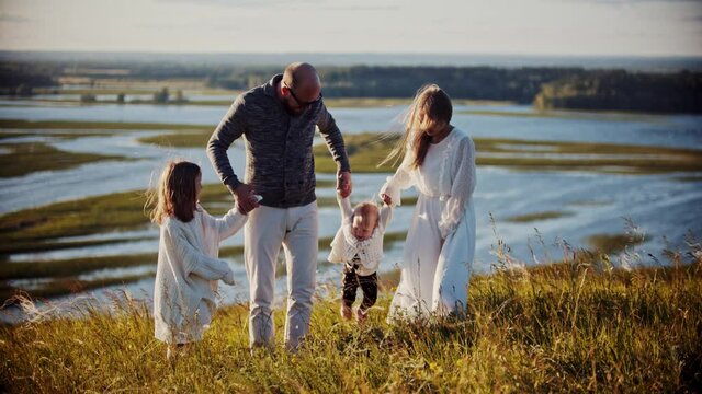 Young family standing on the field - father and mother holding hands with their baby and swinging her forward and backward