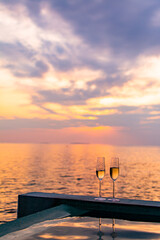 Fototapeta premium Enjoying two glasses of champagne in a pool watching sunset in the ocean