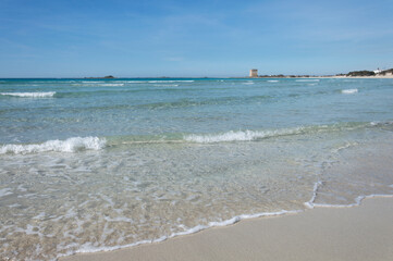 Spiaggia bianca con mare trasparente e torre costiera sullo sfondo