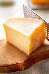 Close-up of a piece of cheese. Piece of parmesan on a wooden board. Cheese grater.