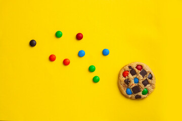 galleta con  chips de chocolate de colores sobre un fondo amarillo con espacio para copi