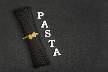 Raw uncooked black cuttlefish ink spaghetti and word Pasta on grey background.