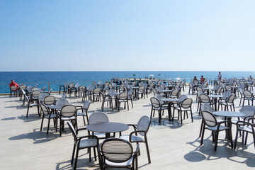 Summer time. The open air cafe with a sea view. White tables and chairs with black edges near the sea. Horizontal orientation.