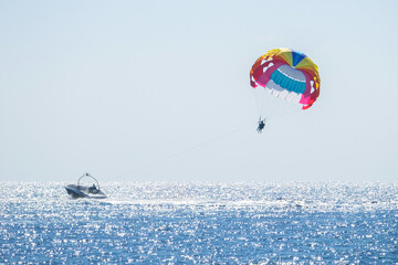 Parasailing in the sea. Small motor boat pulling a multicolored parachute with a couple of people. Selective focus. Horizontal orientation. - Powered by Adobe