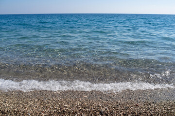 Blue sea water splashing on a gravel beach. View from the beach. The Mediterranean Sea. Horizontal view.