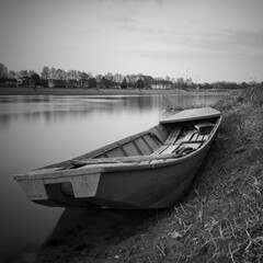 An old fishing boat stranded on the bank of the Sava River in Bosanski Brod, Bosnia and Herzegovina. Black and white picture of a boat in the mud by the river.