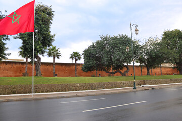 Scenic view of the national flag of Morocco in the center of Rabat. Historic old wall with trees in the background.