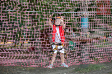 A cute preschool girl goes through an obstacle in the form of a wicker mesh, active leisure, play...
