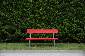 Rote Sitzbank vor einer Hecke im Park