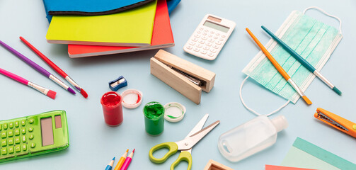 Coronavirus spread prevention measure at school. Surgical mask, alcohol disinfection gel and stationery on pastel blue background,