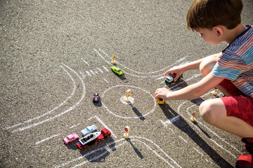 Funny kid boy having fun with picture drawing traffic car with chalks. Creative leisure for children outdoors in summer. Difficult traffic rules concept