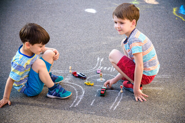 Naklejka premium Two brothers sibling kid boy having fun with picture drawing traffic car with chalks. Creative leisure for children outdoors in summer. Difficult traffic rules education friendship concept