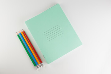 stack of thin student notebooks with colored pencils