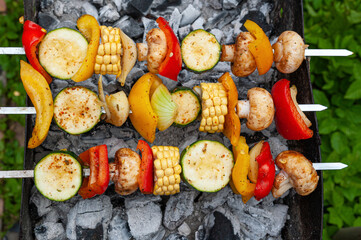 Variety of vegetable ingredients put on metal skewers and placed over charcoal grill.