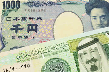 A macro image of a Japanese thousand yen note paired up with a green and yellow on riyal bank note from Saudi Arabia.  Shot close up in macro.
