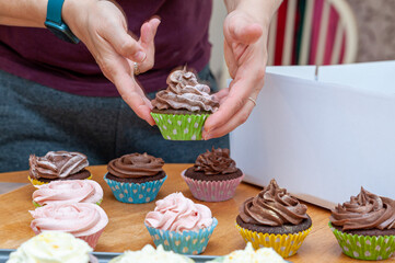Female hands placing beautifully decorated with buttercream on top home baked cupcakes into carton transport box.