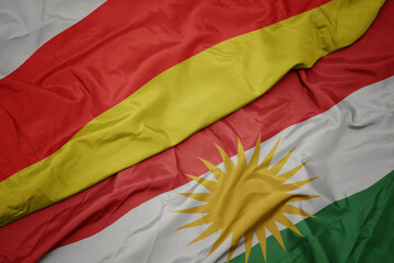 waving colorful flag of kurdistan and national flag of south ossetia.