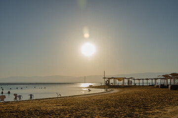 sunrise over the sea with sandy beach sun canopies on the shore in the background mountains in the haze