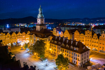 Starry evening over Jelenia Gora market square. Beautiful illuminated town hall building, old tenement houses and restaurants around central place. In a distance surrounding mountains