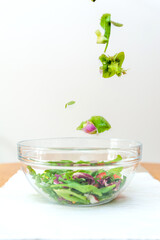 Pieces of fresh vegetables falling down into glass bowl creating healthy salad.