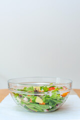 Pieces of fresh vegetables falling down into glass bowl creating healthy salad.