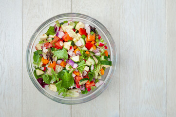 Fresh and healthy vegetables for salad in a glass bowl placed on white wooden surface.