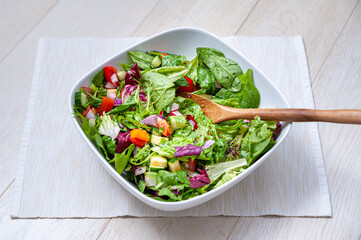Fresh and healthy vegetables in a white square bowl placed on white wooden surface.