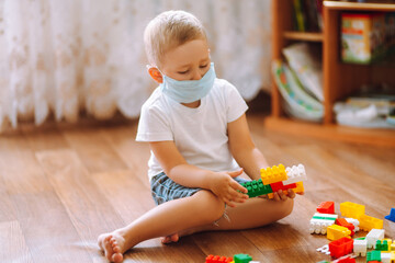 Little boy in sterile medical mask  playing constructor at home. The concept of preventing the spread of the epidemic.