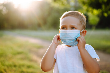 Portrait of little boy with medical face mask in the park during pandemic. Concept of health and safety life from coronavirus. Covid-2019. Kids safety.