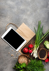 Farm food products on chopping board with tablet computer and shopping paper bag. Top view.