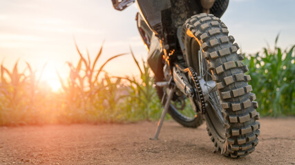 Part of a dirt bike on a dirt road in a cornfield with warm light.