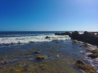 beach and rocks with waves rolling in and blue sky at Little Corona Beach in California