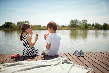 cute minor couple sitting by the river eating watermelon