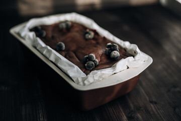 
brownie cake garnished with frozen blackcurrant berries in a brown mold with white parchment on a dark background