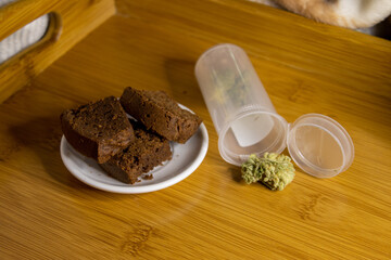Cannabis brownies on a wooden tray with cannabis buds in a clear plastic tube