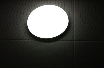 Turned on round glass lamp on the wall in the dark, closeup. White light on a black background. Lighting. Electricity.