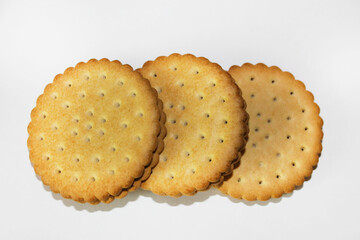 Three round cookies with wavy edges and small holes lie in a horizontal row on a white surface, one on top of the other, close-up. Dessert.