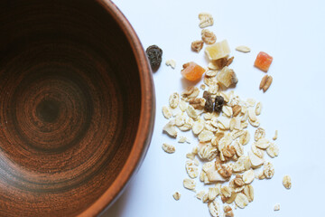 A deep brown clay plate on a pale blue background, top view, close-up. Muesli is scattered around the plate. Cereals with a variety of nuts, pieces of fruit and seeds. Healthy food. Breakfast.