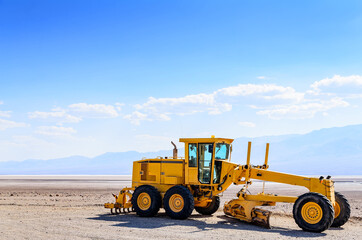 Yellow grader in the desert against the blue sky and mountains